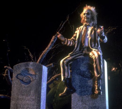 Michael Keaton as Beetlejuice, sitting on a gravestone.