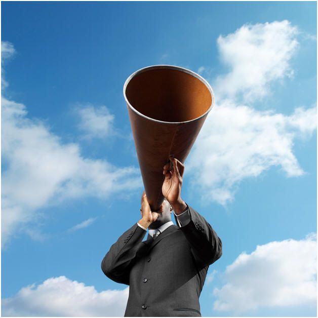 A man in a suit shouting through a cone megaphone.