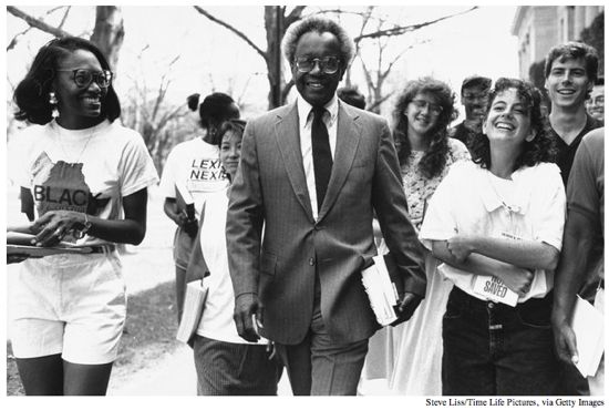 Black and white photo of Derrick Bell walking with a group of Harvard Law students