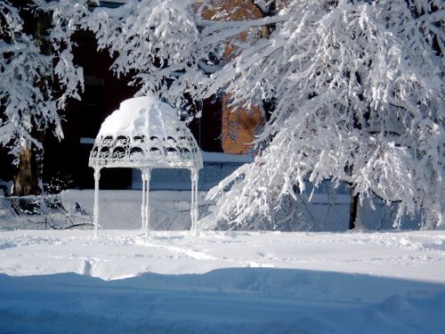 a white metal gazebo buried in snow and a tree